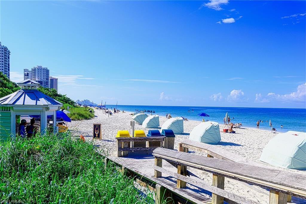 Sandy beach with blue ocean, beach chairs, and a boardwalk beside coastal high-rises.