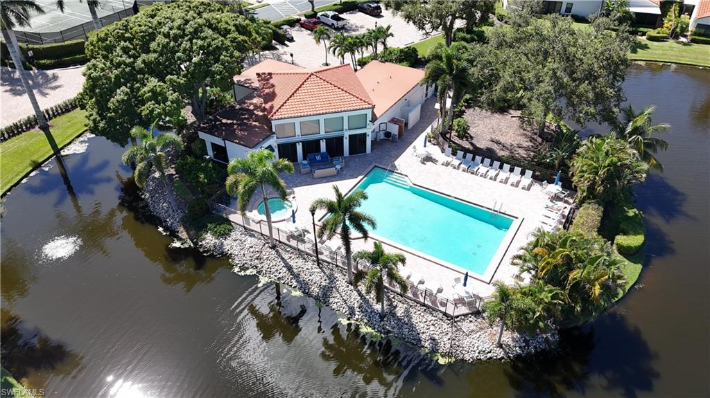 Aerial view of a waterfront clubhouse and turquoise swimming pool surrounded by palms.