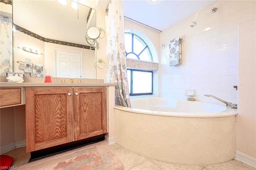 Bathroom with a corner soaking tub beneath an arched window and a wood vanity.