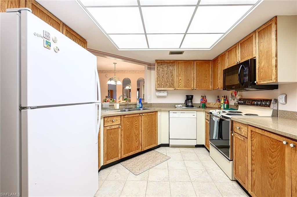 Kitchen with honey-colored wood cabinets, white appliances, and a pass-through to the adjoining room.