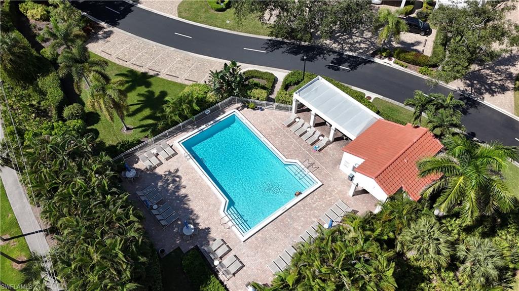 Aerial view of a community pool, brick deck, lounge chairs, and covered pavilion amid palms.
