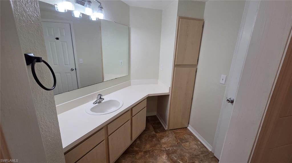 Bathroom with a long white vanity, large mirror, light wood cabinetry, and brown stone-pattern tile.