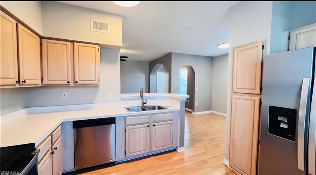 Kitchen with light wood cabinets, white counters, stainless appliances, and an open connection to the adjoining room.