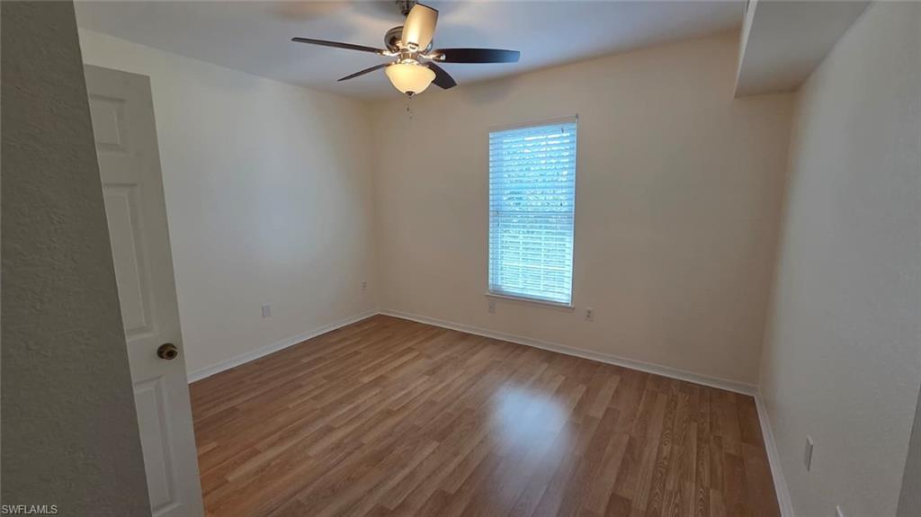 Vacant bedroom with wood-look flooring, a ceiling fan, and a window with blinds.