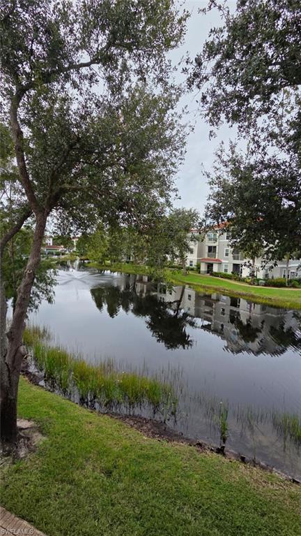Condominium buildings reflected in a calm canal, framed by mature trees and grassy banks.