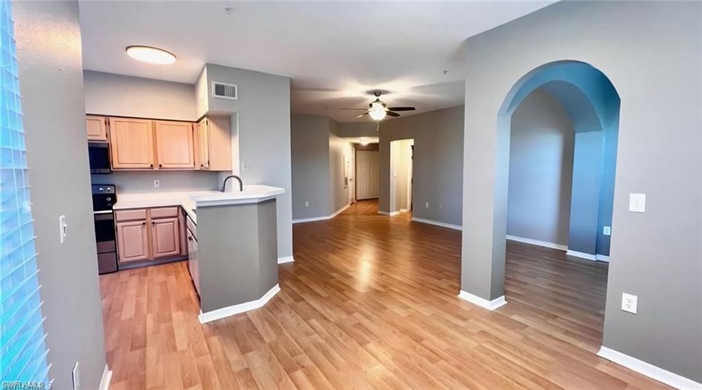 Open-plan condo kitchen and living area with a white peninsula, wood cabinets, and arched doorway.