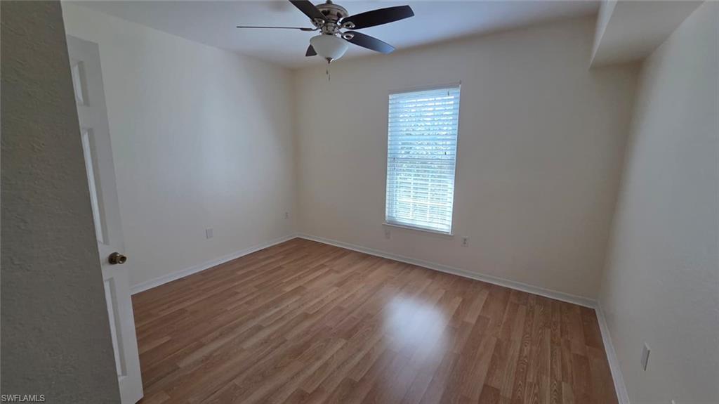 Empty bedroom with wood-look flooring, a ceiling fan, and a window with blinds.