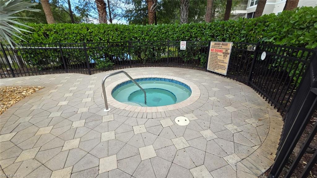 Outdoor jacuzzi with a stainless-steel handrail, circular brick border, and fenced paved deck.