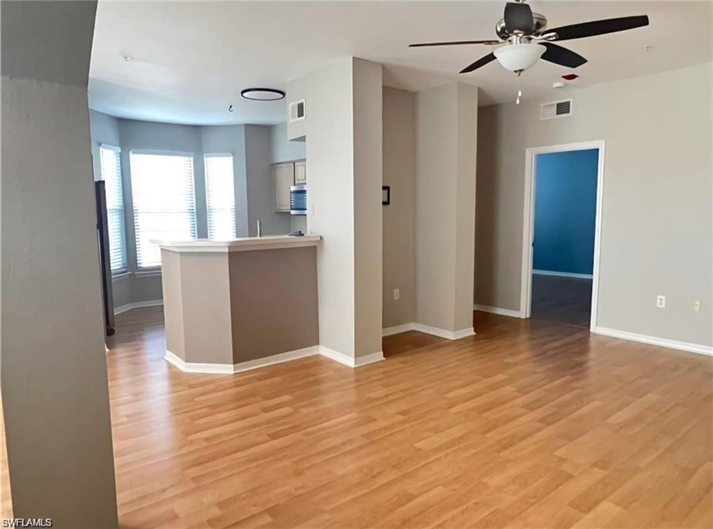 Unfurnished living area with wood-look floors, a kitchen peninsula, and a doorway to a blue room.