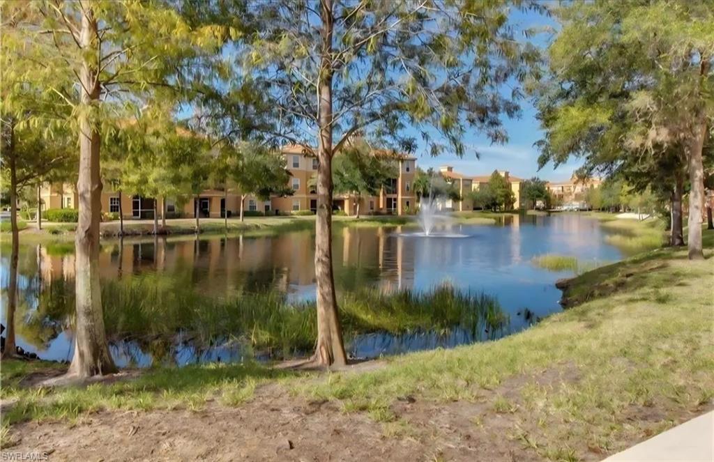 Residential buildings across a landscaped pond with a fountain and mature trees.