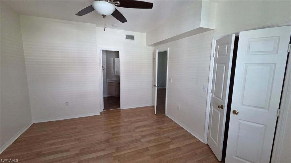 Vacant bedroom with wood-look flooring, a ceiling fan, and open doorways.