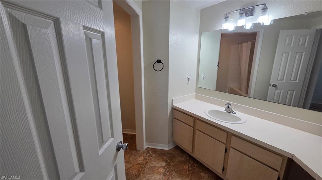 Bathroom vanity with a single sink, large mirror, and brown patterned tile floor.