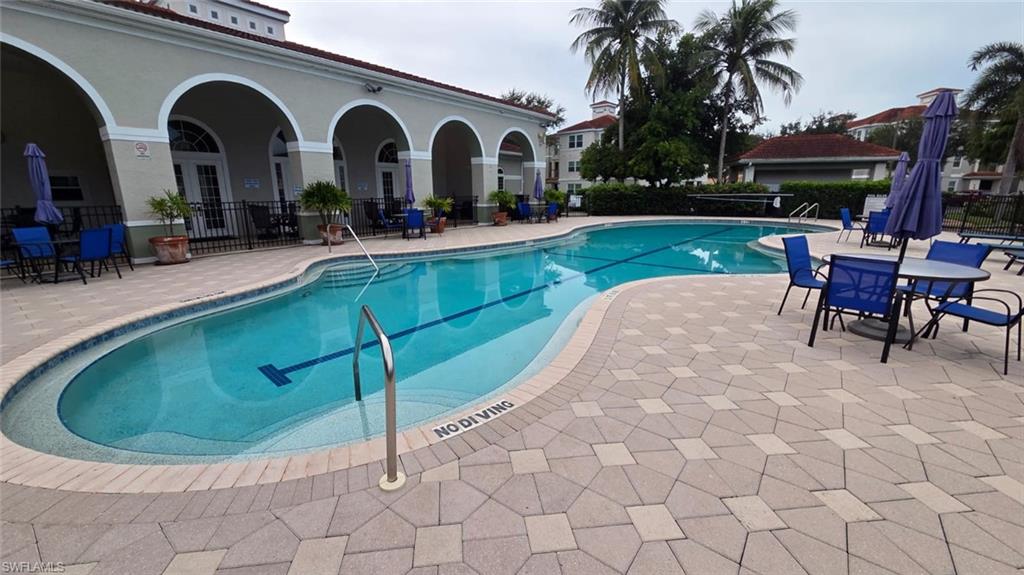 Community pool with a curved shape, arched walkway, and blue patio seating.