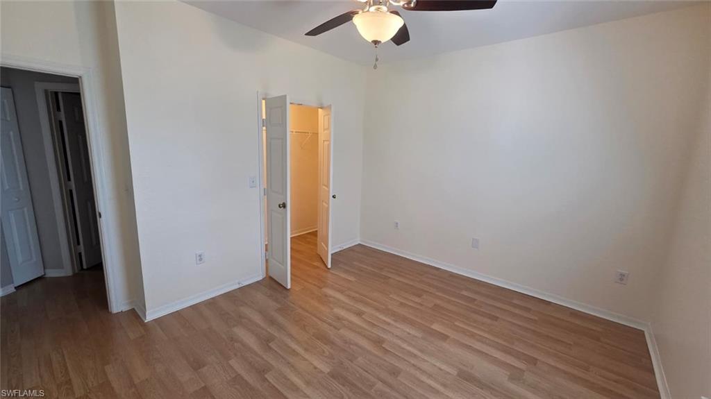 Vacant bedroom with wood-look flooring, ceiling fan, and open closet.