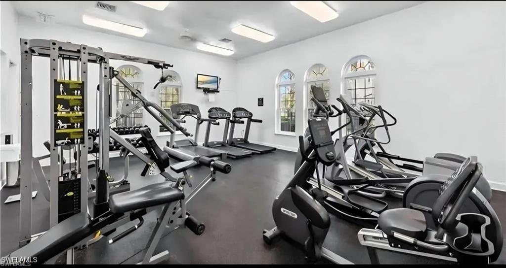 Fitness room with weight machines, treadmills, elliptical trainers, and arched windows.