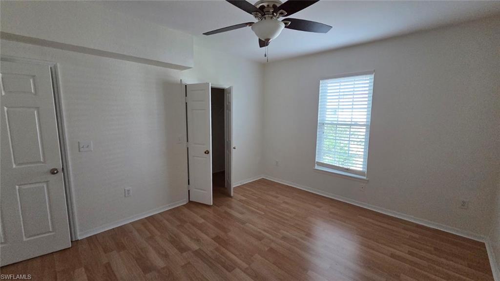 Empty bedroom with wood-look flooring, a ceiling fan, and a window with blinds.