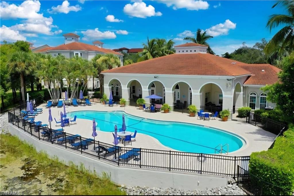 Community pool with lounge chairs and umbrellas beside a white arched clubhouse.