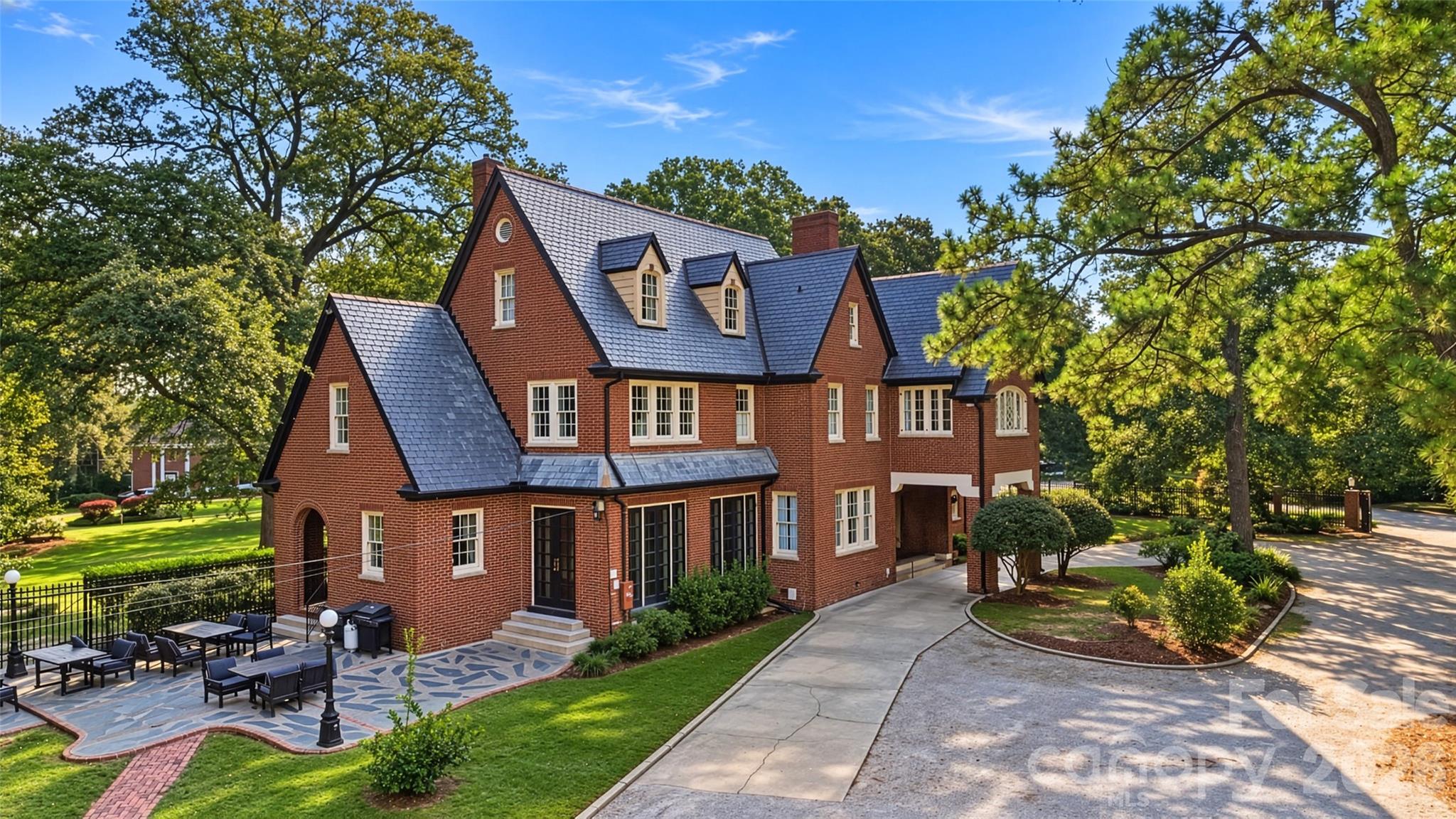 Red-brick house with a slate roof, landscaped grounds, and a stone patio with outdoor seating.