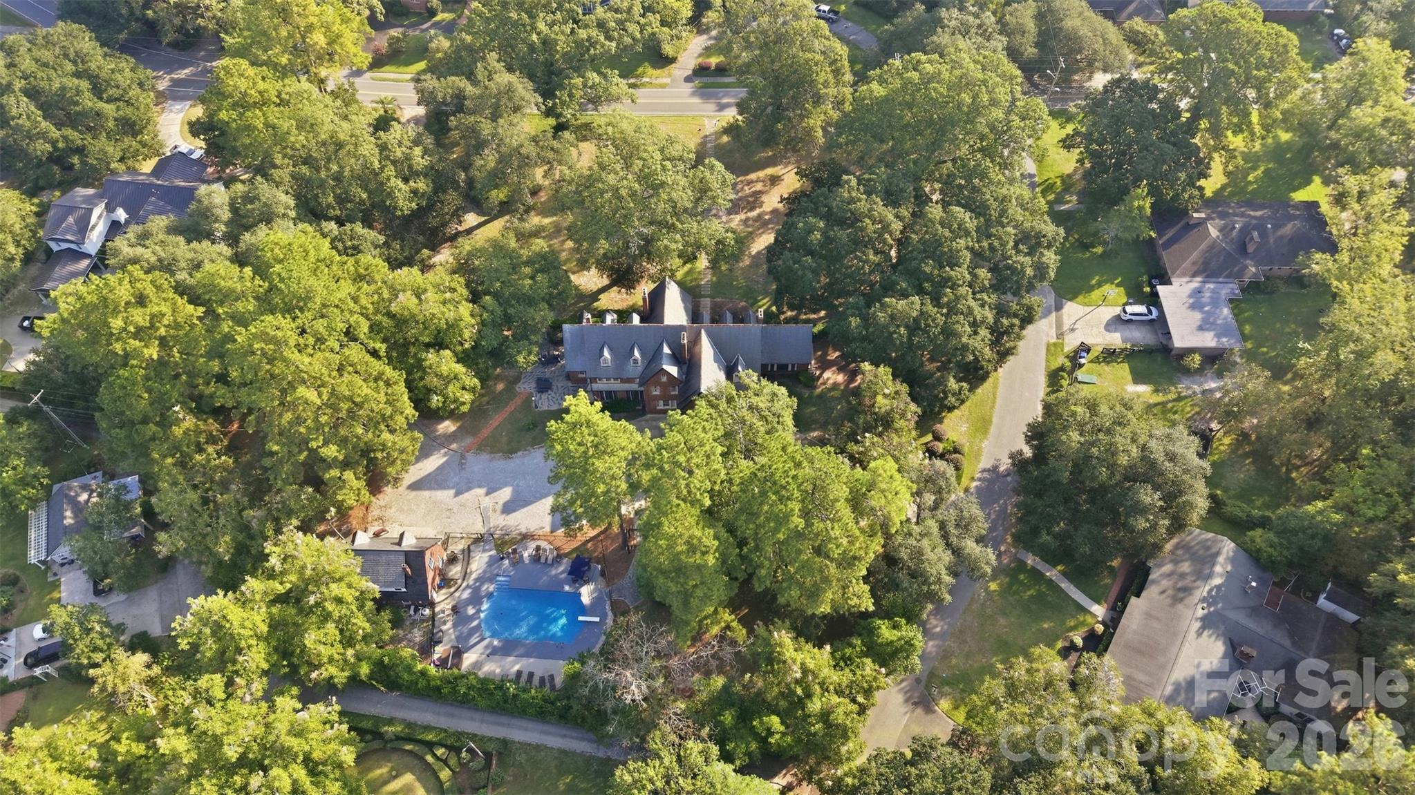 Aerial view of a tree-surrounded home with a swimming pool and paved outdoor area.