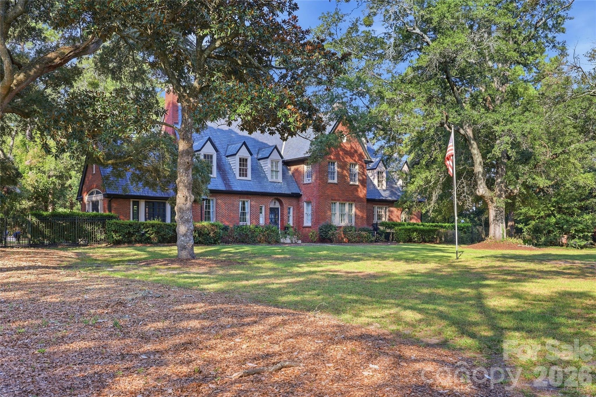 Red-brick house with slate-blue roof and dormer windows, framed by mature trees and a broad lawn.