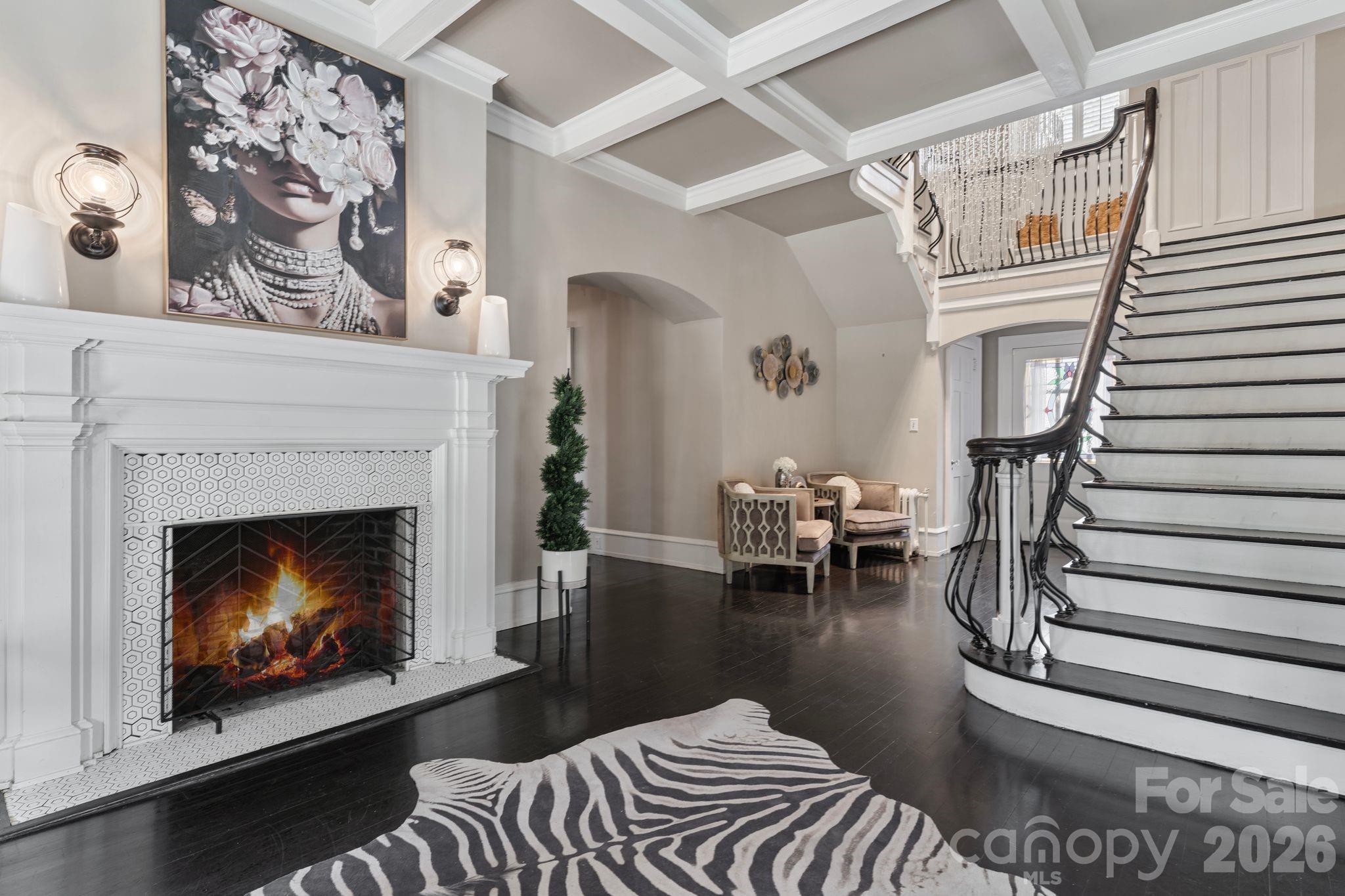 Two-story foyer with a sweeping staircase, lit fireplace, and zebra-patterned rug.