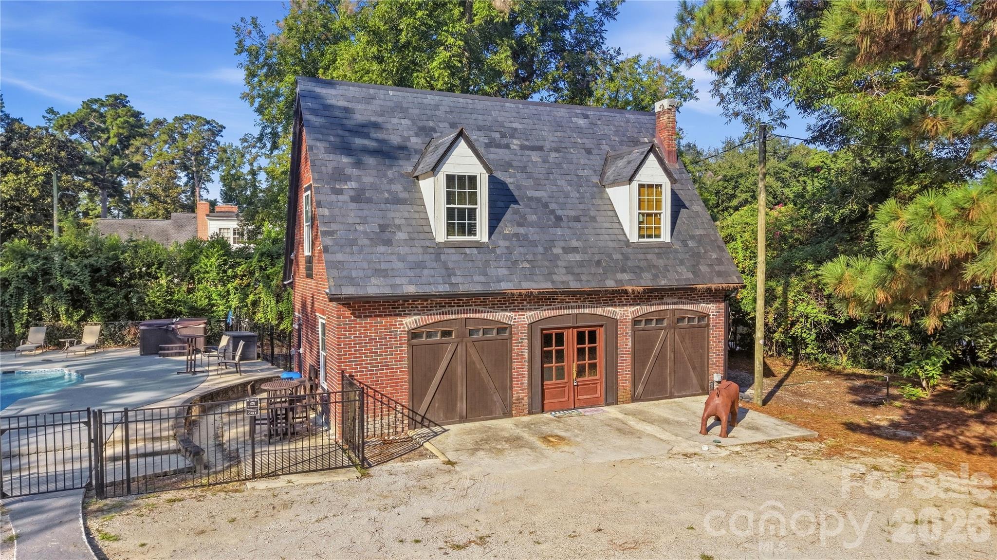 Brick pool house with a steep slate roof beside a fenced swimming pool and patio.