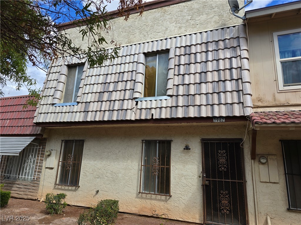 Two-story stucco residence with a gray tiled upper facade and decorative metal security gate.