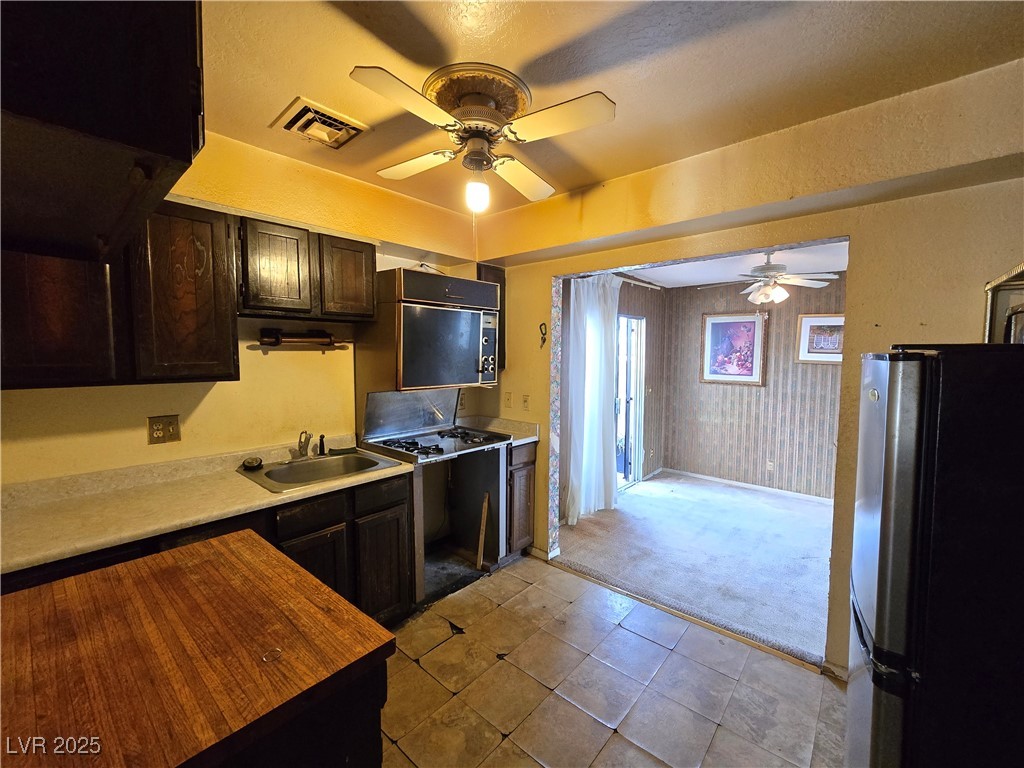 Kitchen with dark wood cabinets and tiled floor opening into a carpeted room.
