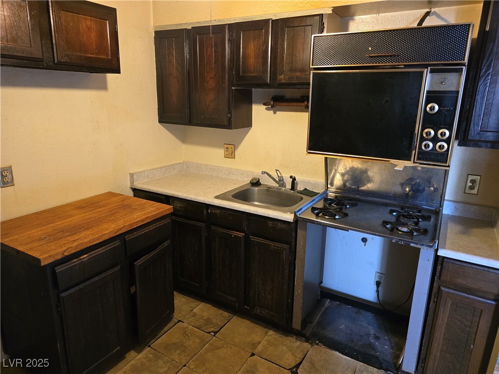 Kitchen with dark wood cabinets, worn tile, and an older range beside a double-basin sink.