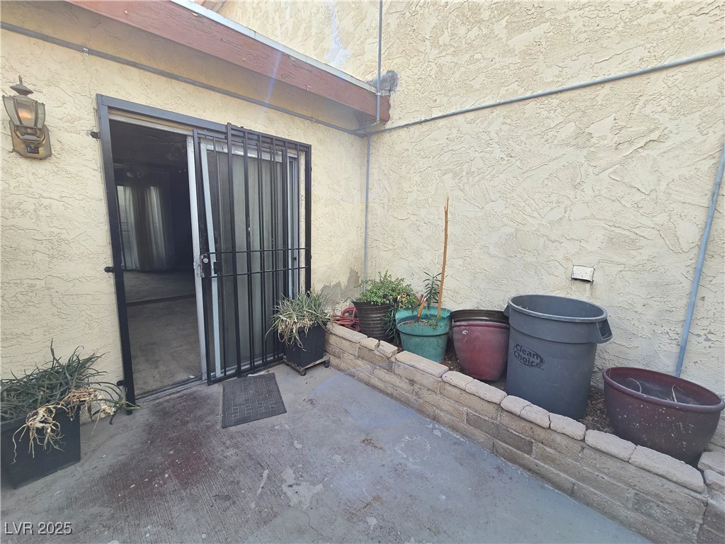 Enclosed concrete patio with a barred sliding door and potted plants along the stucco wall.