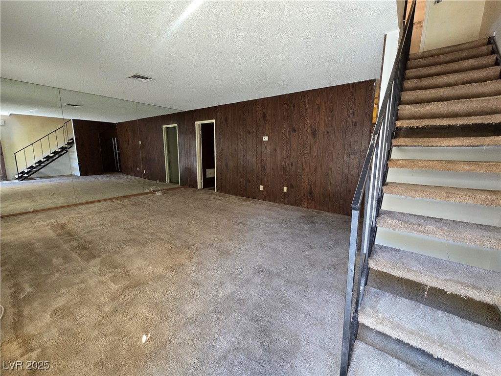 Vacant living room with a mirrored wall, dark wood paneling, and carpeted stairs.