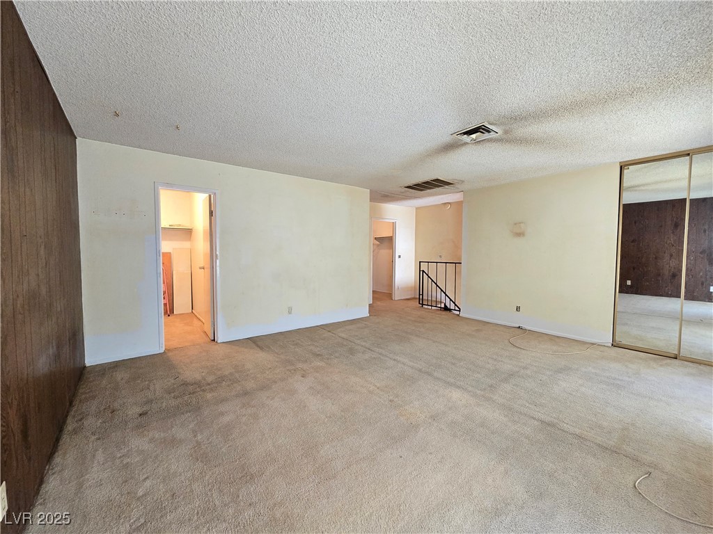 Empty carpeted bedroom with mirrored closet doors and a dark wood-paneled wall.