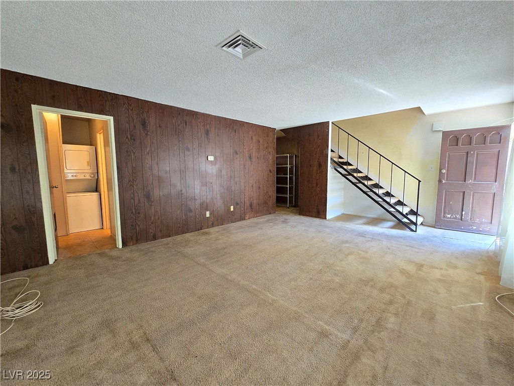 Empty living room with carpet, dark wood-paneled walls, and an open staircase.