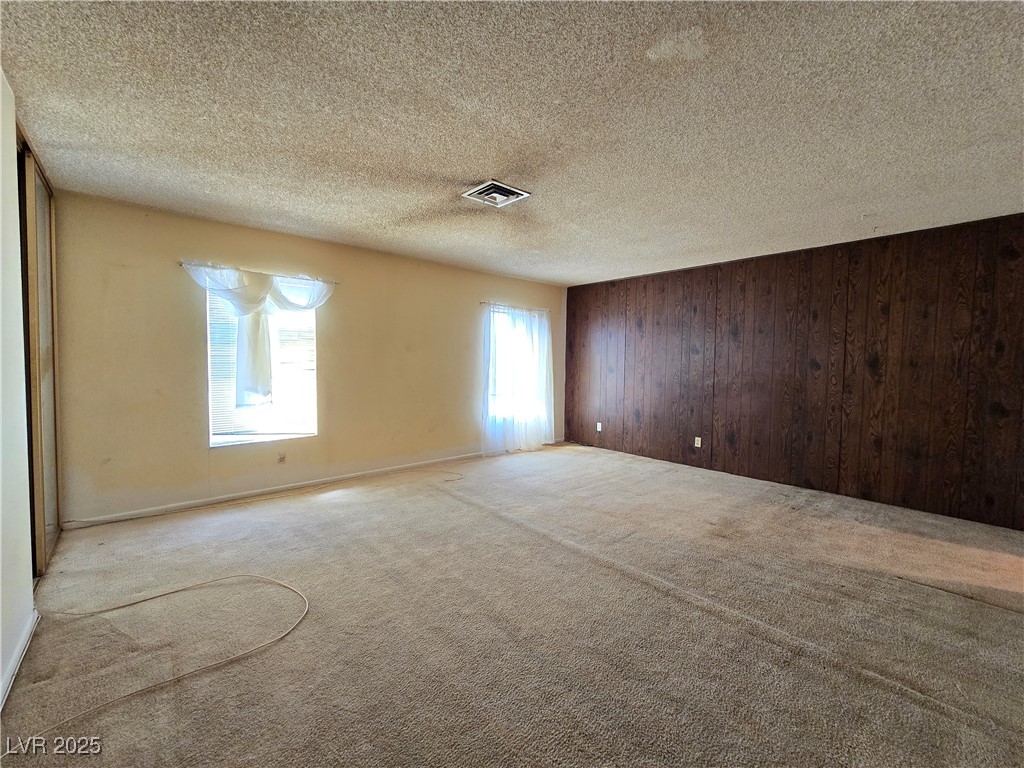Empty living room with beige carpet, a dark wood-paneled wall, and two windows.