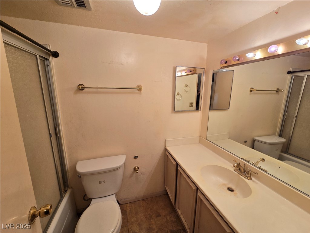 Bathroom with a tub-shower enclosure, toilet, and long vanity beneath a large mirror.