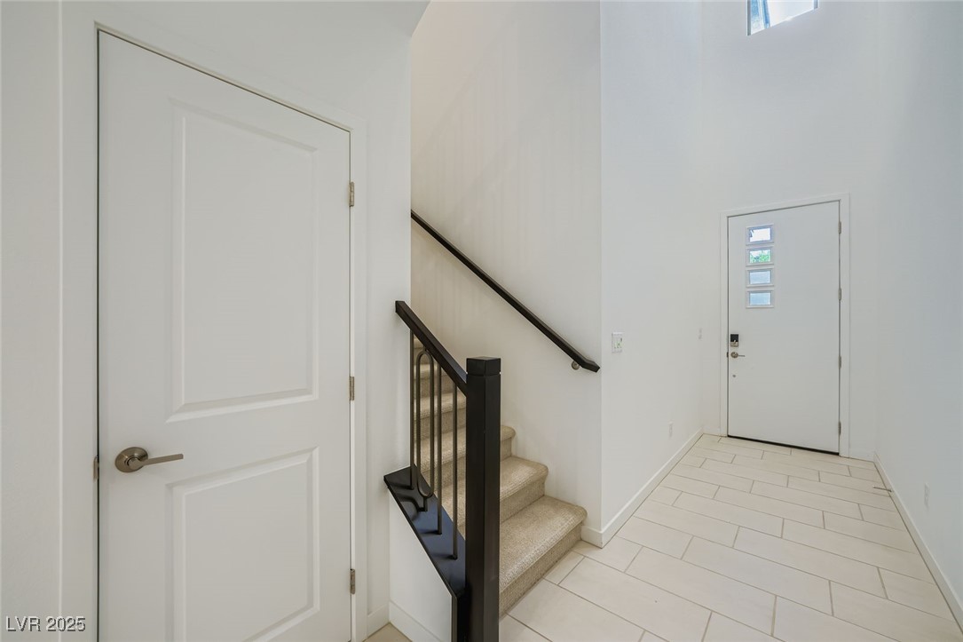 Entry foyer with white tile flooring, a front door, and a carpeted staircase with dark railing.