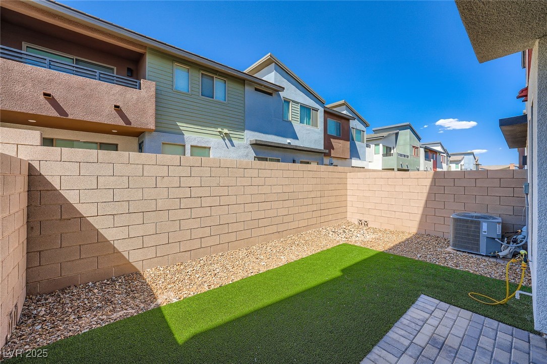 Backyard with artificial grass, gravel landscaping, block walls, and a paved patio.