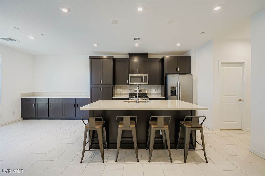 Modern kitchen with dark cabinets, stainless steel appliances, and a large island with four bar stools.