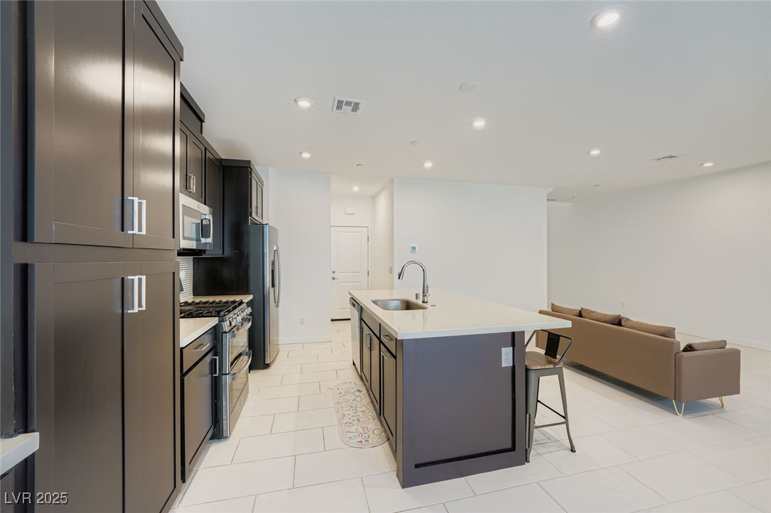 Open-plan kitchen with dark cabinets, stainless steel appliances, a white island, and a tan sofa.