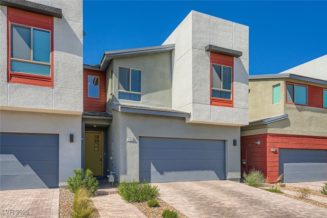 Modern two-story home with red window accents, a gray double garage, and a paved driveway.