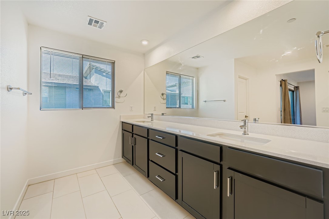 Bathroom with a long dark vanity, two sinks, a wall-length mirror, and a window with blinds.