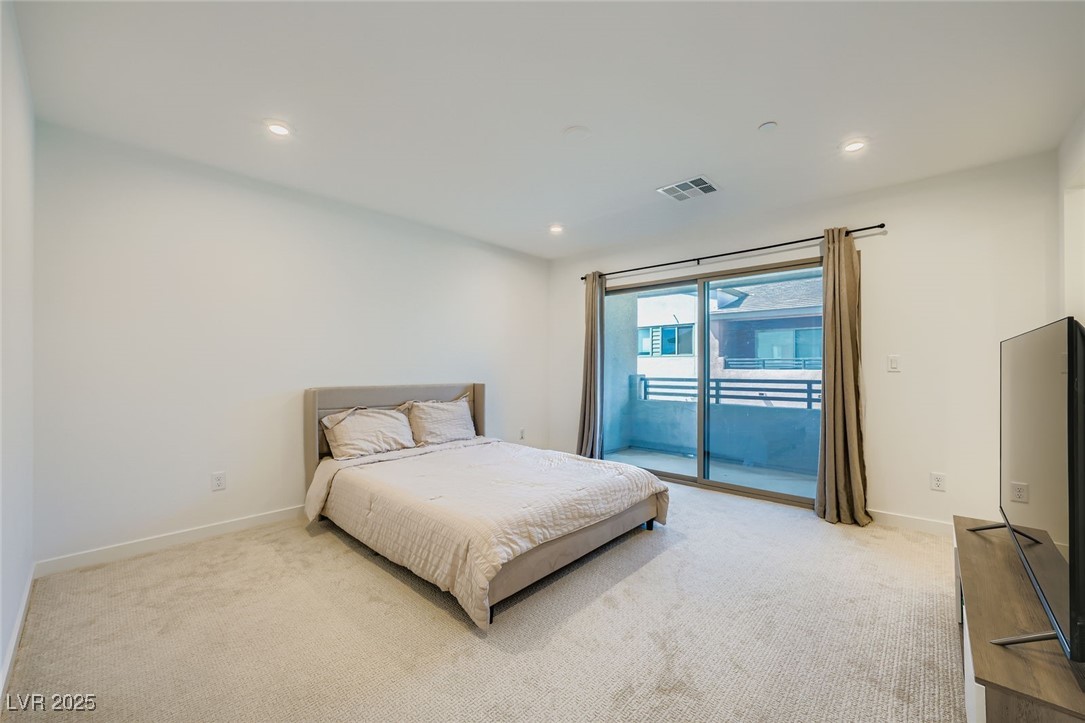Bedroom with a white bed, beige carpet, and sliding glass doors to a balcony.