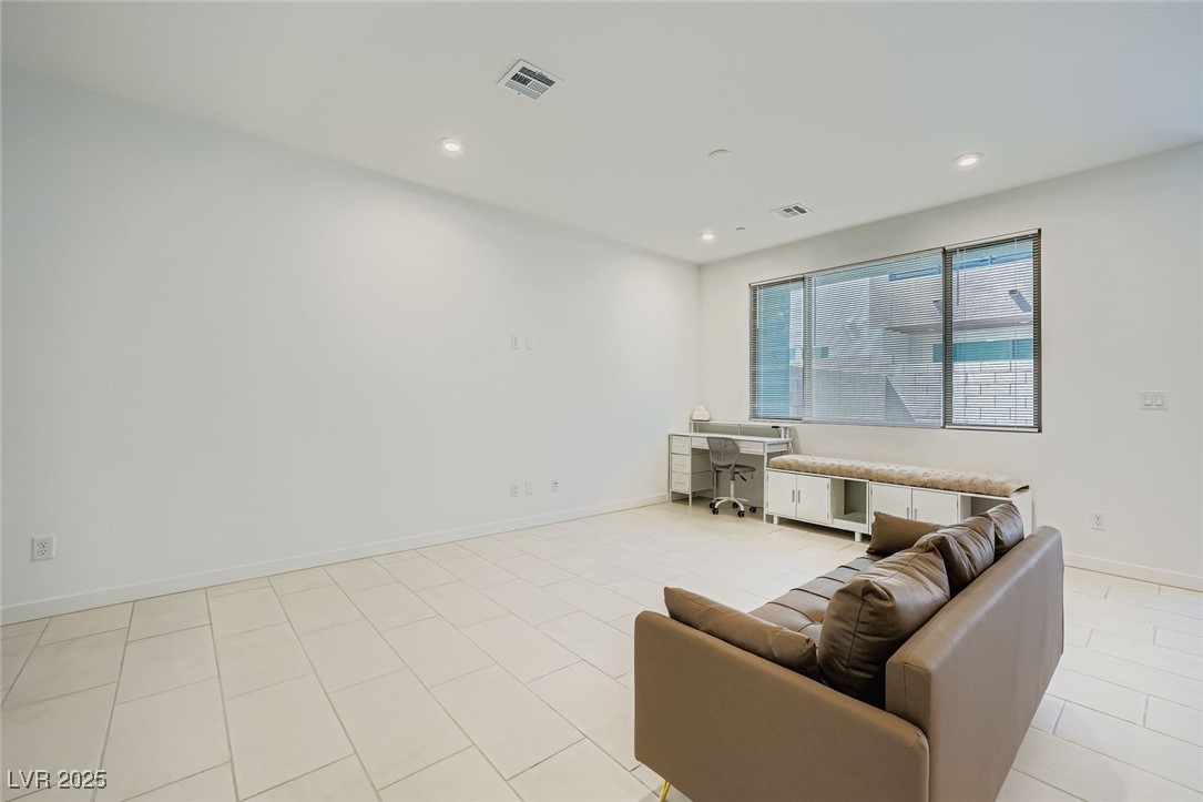 Living room with a brown sofa, tiled floor, window bench, and desk by the windows.