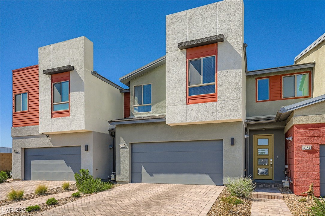 Modern two-story stucco home with red accents, a wide garage, and desert landscaping.