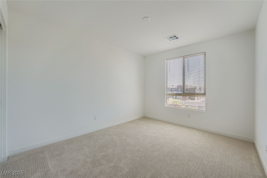 Empty carpeted bedroom with white walls and a window fitted with blinds.