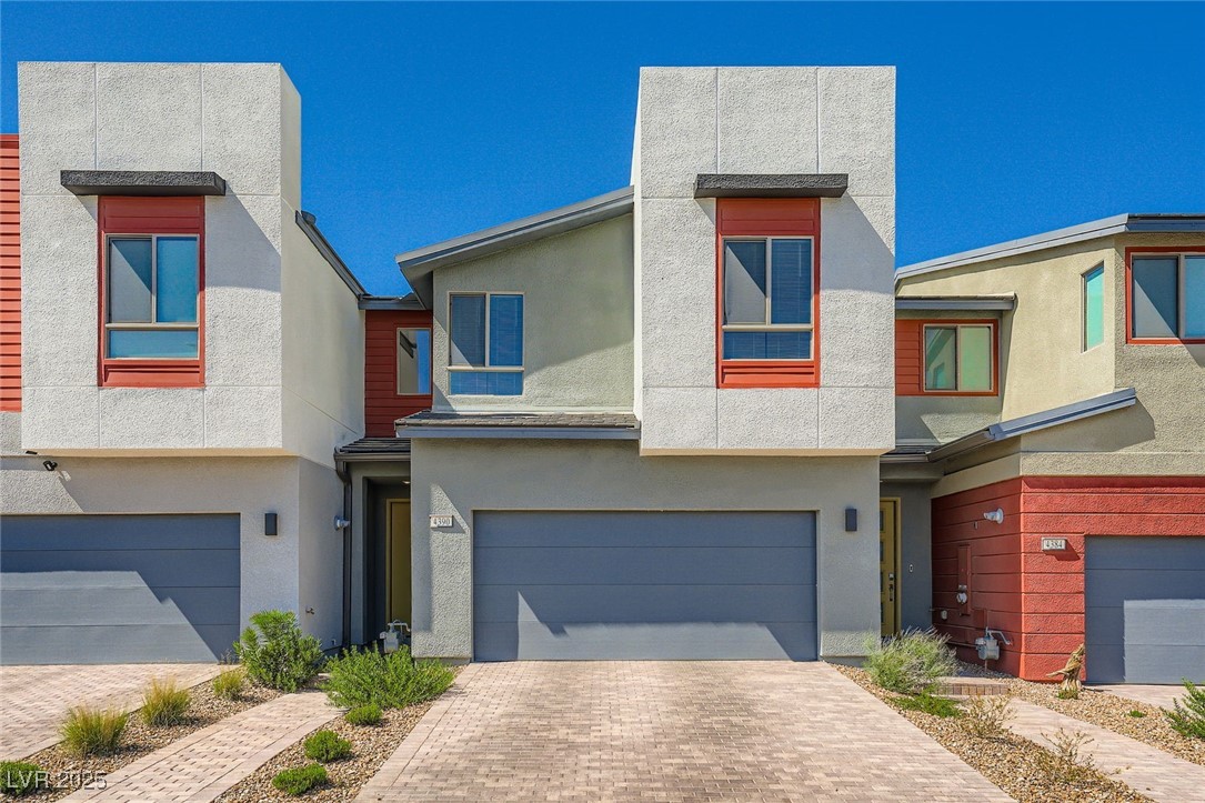 Modern two-story townhouse with red-trimmed windows, a two-car garage, and a brick-paver driveway.