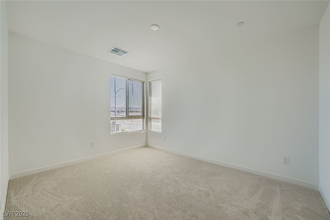 Empty carpeted room with corner windows and blinds.