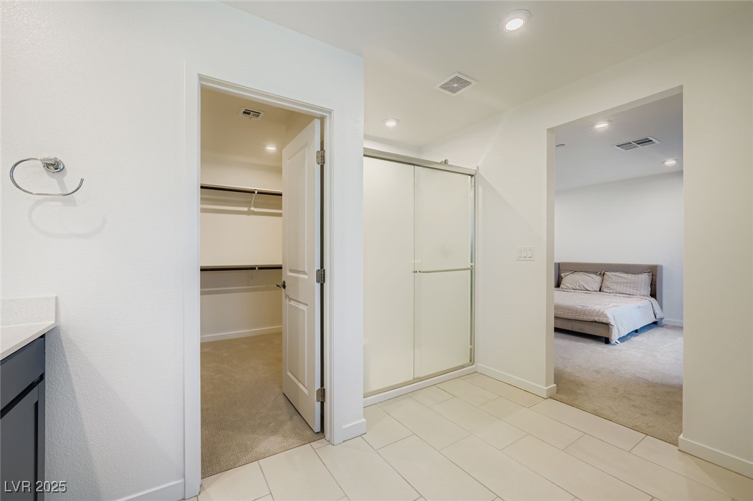 Primary bathroom with glass shower enclosure, walk-in closet doorway, and bedroom visible beyond.