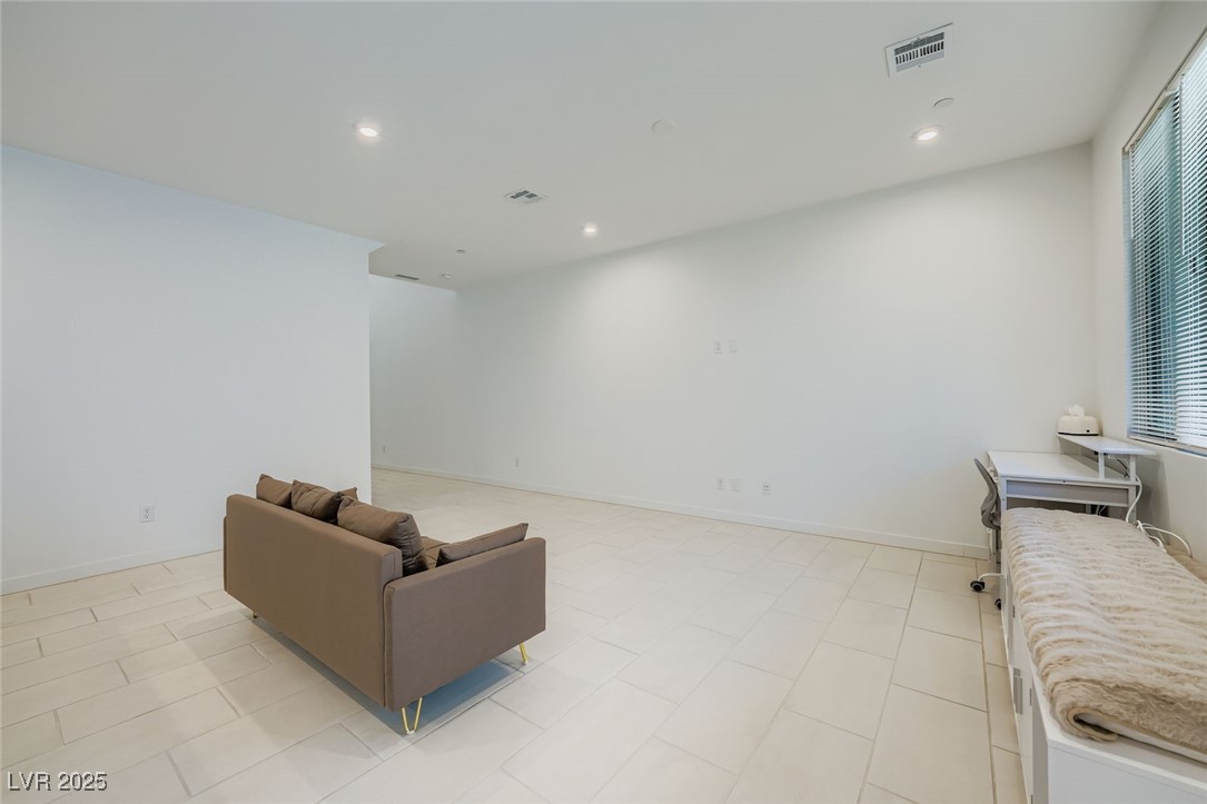 Spacious tiled living area with a brown sofa and a daybed beside a window.