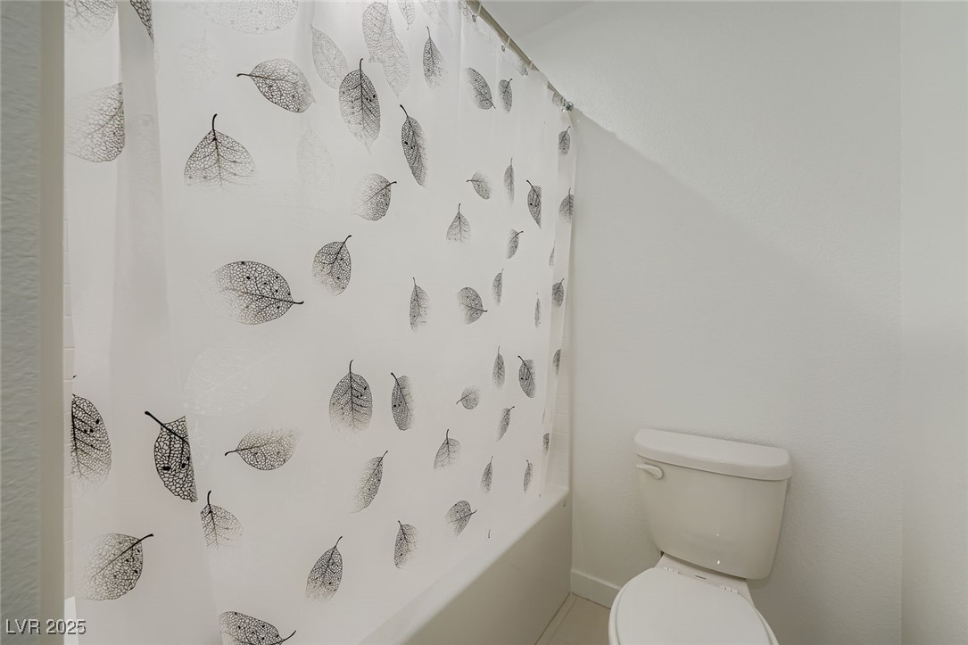 White bathroom with a toilet beside a bathtub and a black leaf-patterned shower curtain.